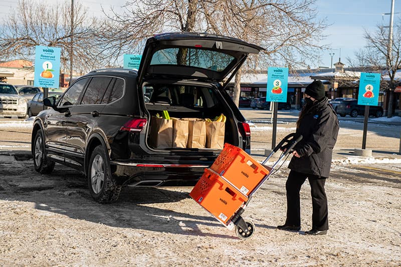 An image representing Voilà by Safeway teammate delivering grocery order in designated Safeway curbside pickup parking spot.