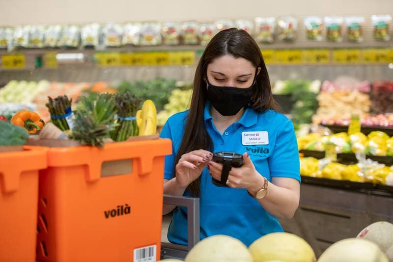 An image representing Voilà by Safeway teammate using handheld device to assemble curbside pickup order.