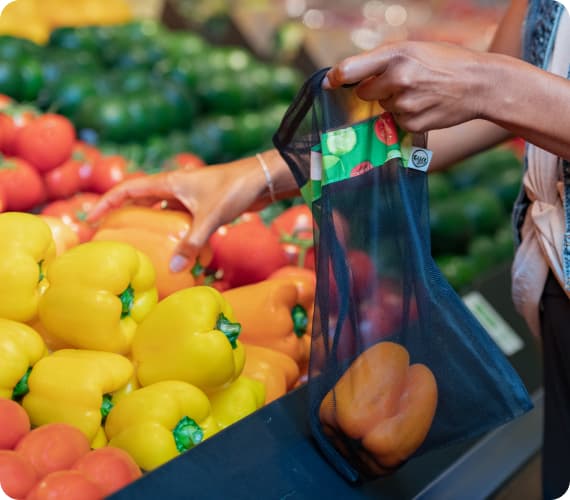 An image of a woman picking up fresh vegetables from the grocery store.